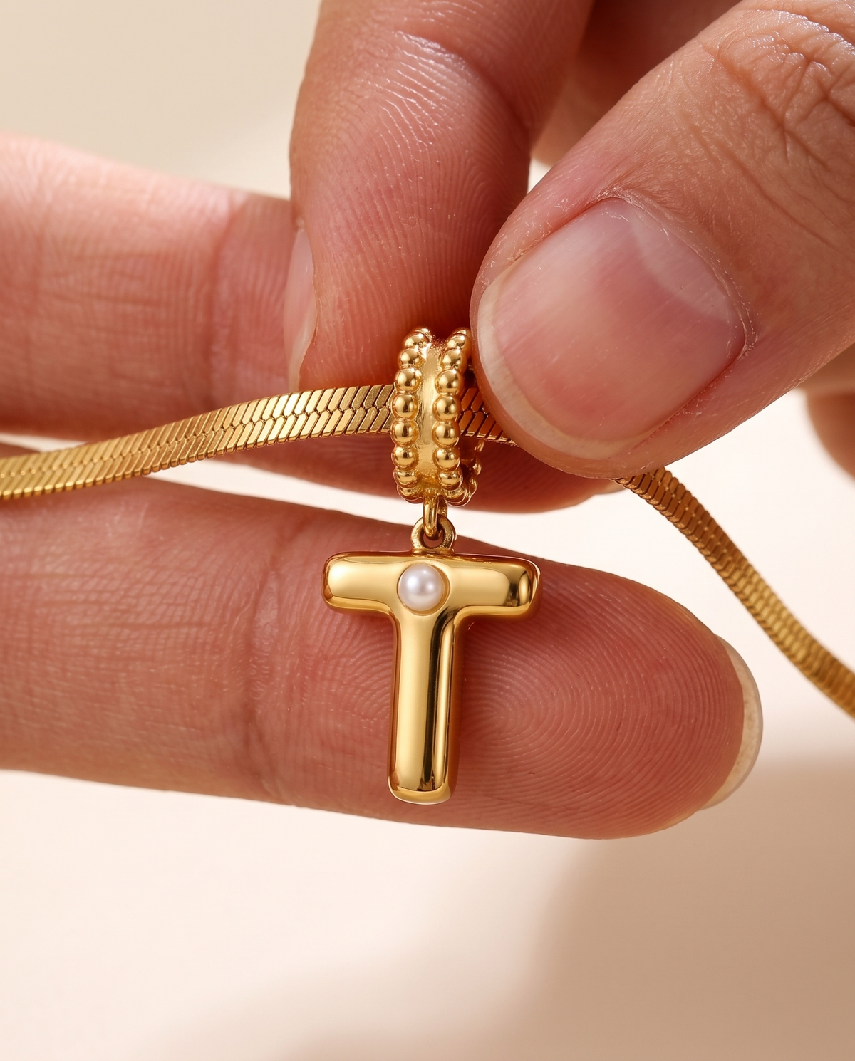 Collana Alma con lettera T in acciaio 316L PVD oro, perlina nella curva