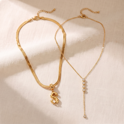 Il Look Alma: la collana con iniziale e perla e la collana a Y con zirconi appoggiate insieme su lino crema