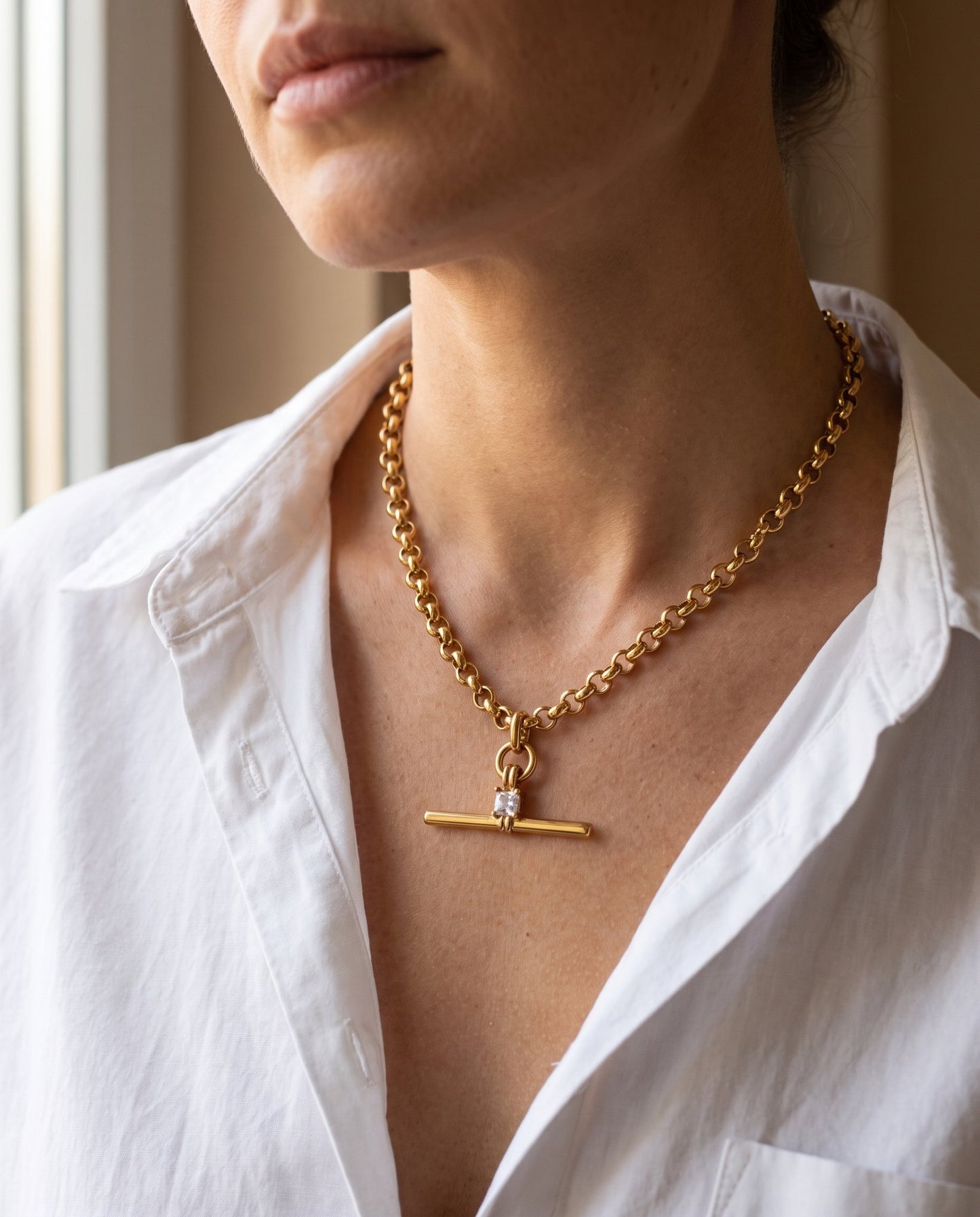 Collana Isla indossata: T-bar con zircone quadrato appoggiata alla base del collo, su camicia bianca