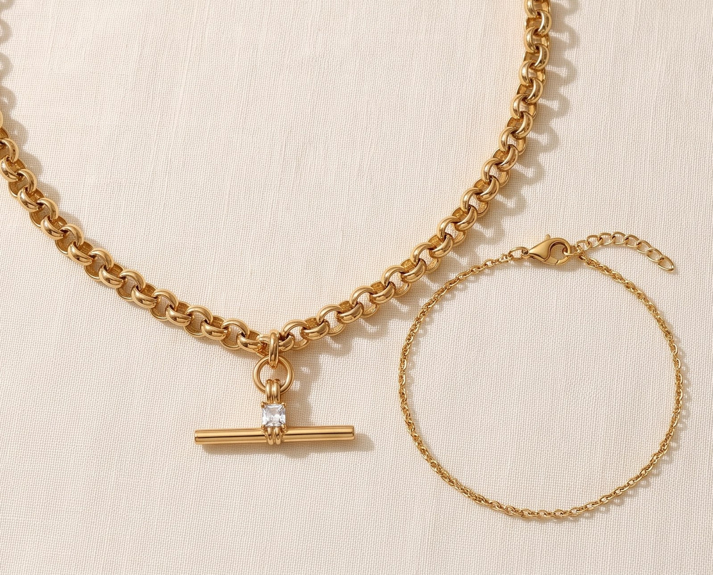 Il Look Isla: la collana T-bar con zircone e il bracciale a catena sottile appoggiati insieme su lino crema