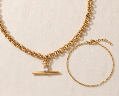 Il Look Isla: la collana T-bar con zircone e il bracciale a catena sottile appoggiati insieme su lino crema